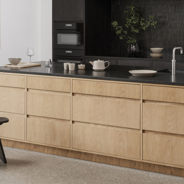 Modern minimalist kitchen with wood cabinetry and sleek black countertops.