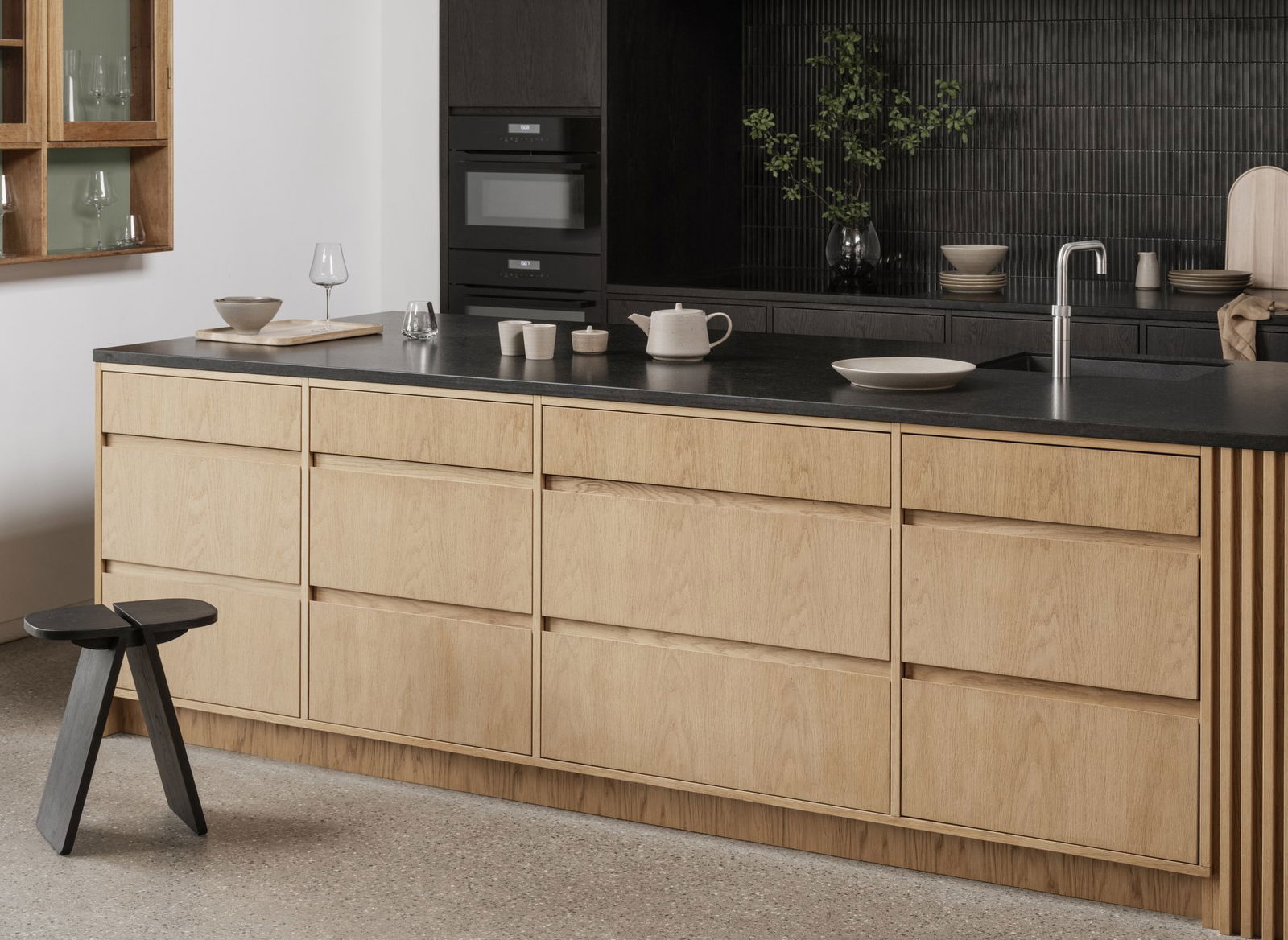 Modern minimalist kitchen with wood cabinetry and sleek black countertops.