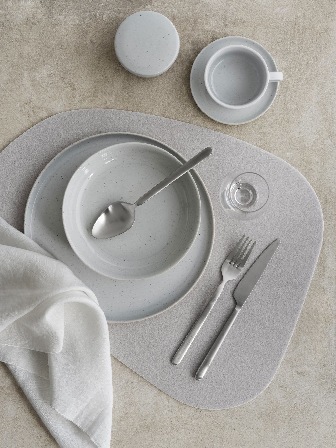 Elegant dining setting with gray tableware, cutlery, and a linen napkin on a neutral surface.
