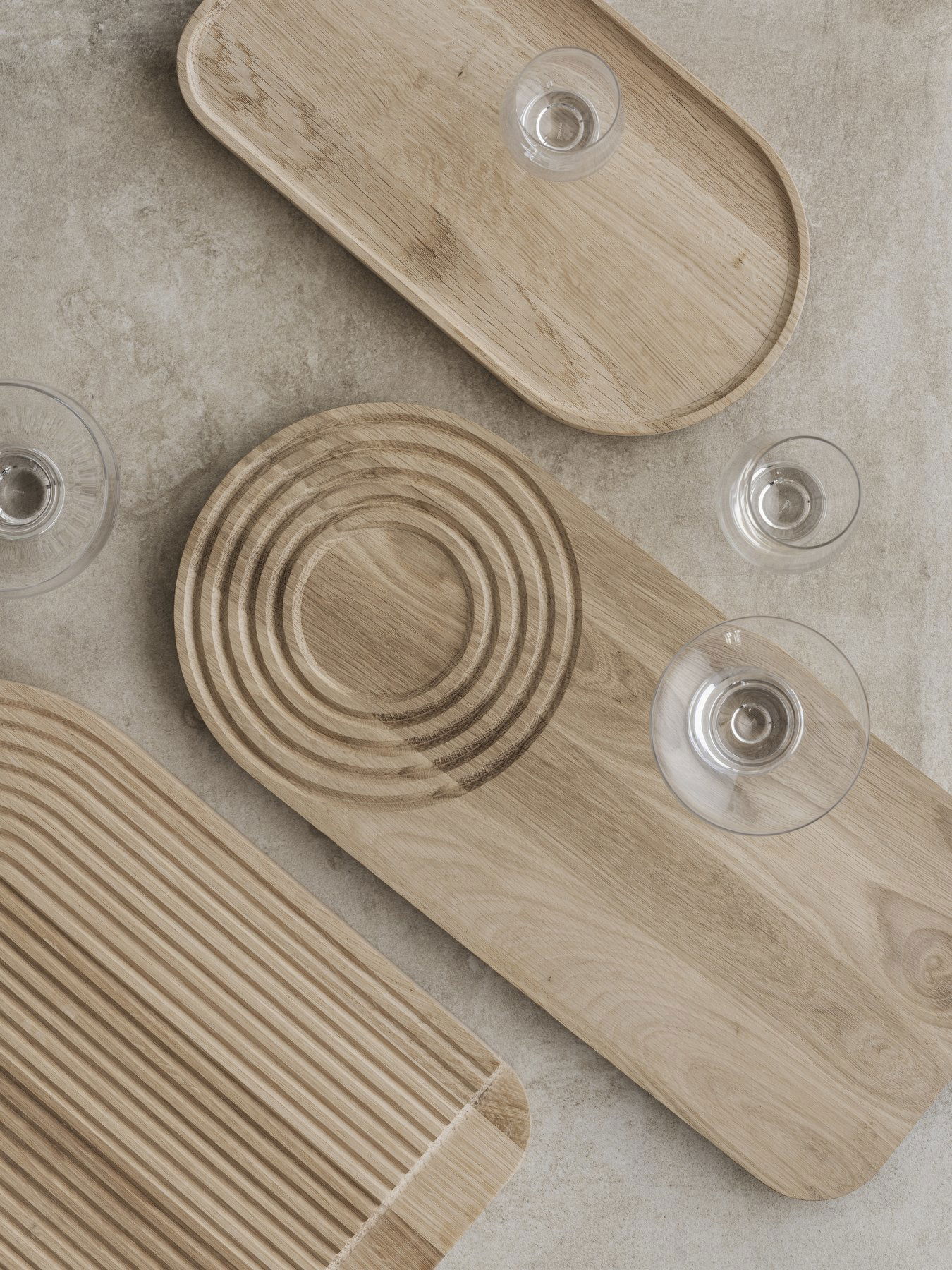Stylische Holzserviertabletts mit eleganten Glaswaren auf einer neutralen Steinoberfläche.