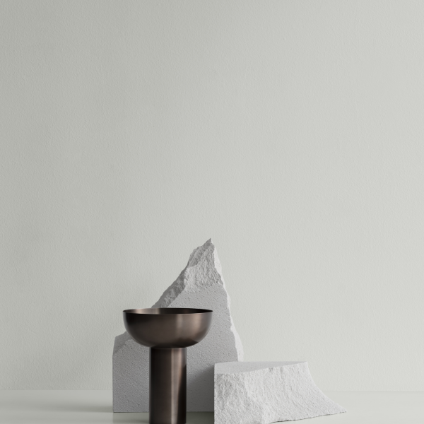 Minimalistische Dekoration mit einer Bronze-Schüssel und strukturierten weißen Steinen vor einem sanften grünen Hintergrund.