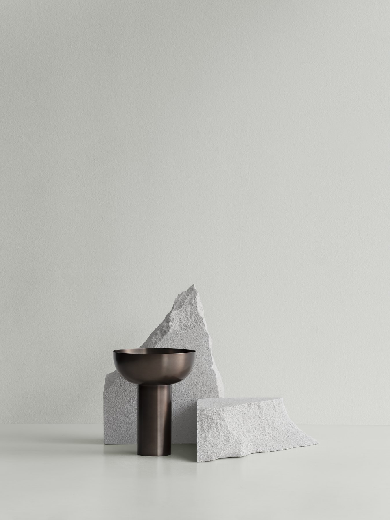 Minimalistische Dekoration mit einer Bronze-Schüssel und strukturierten weißen Steinen vor einem sanften grünen Hintergrund.