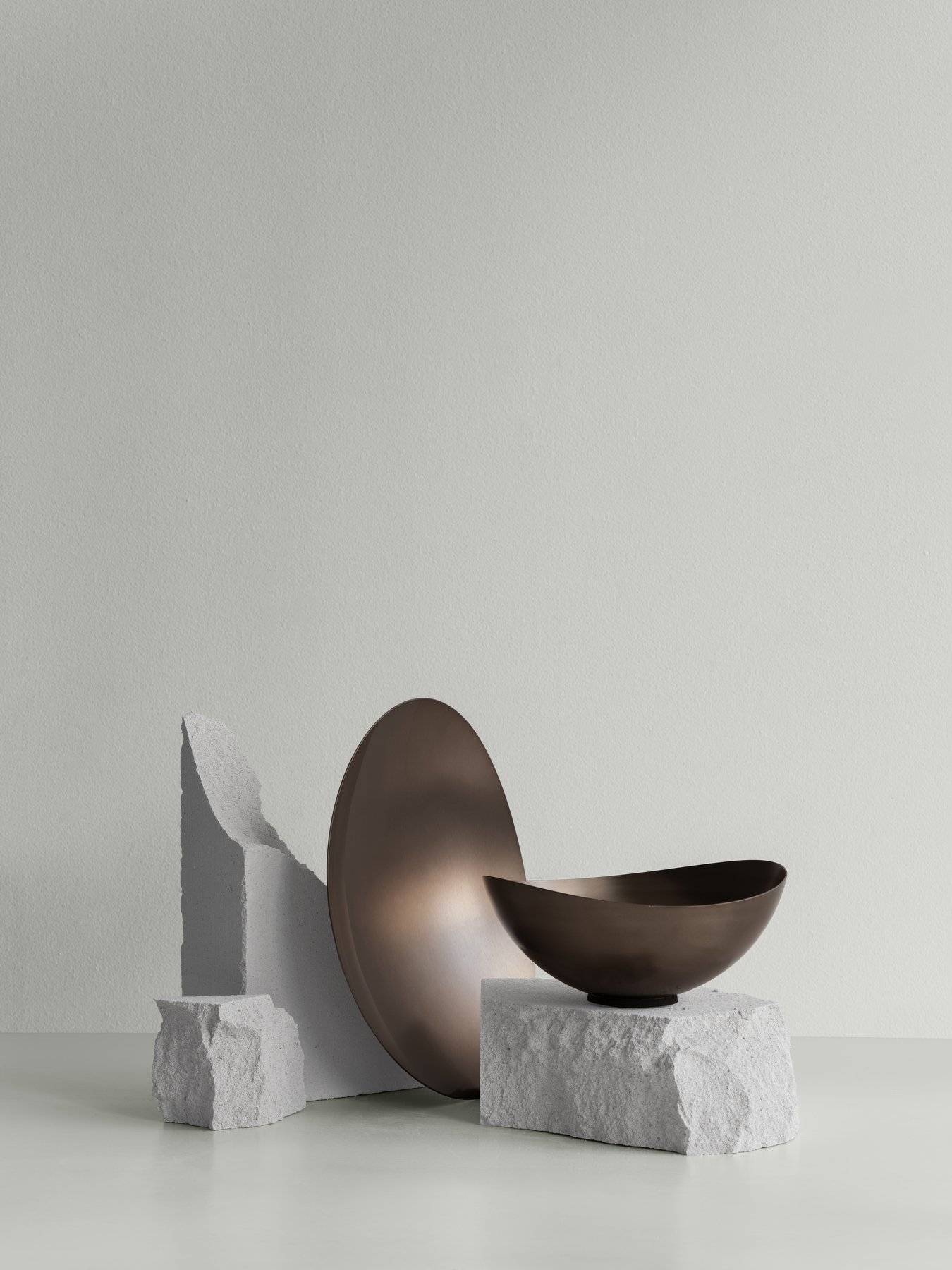 Moderne Bronze-Schalen, die auf strukturierten Betonblöcken vor einem sanften Pastellhintergrund präsentiert werden.