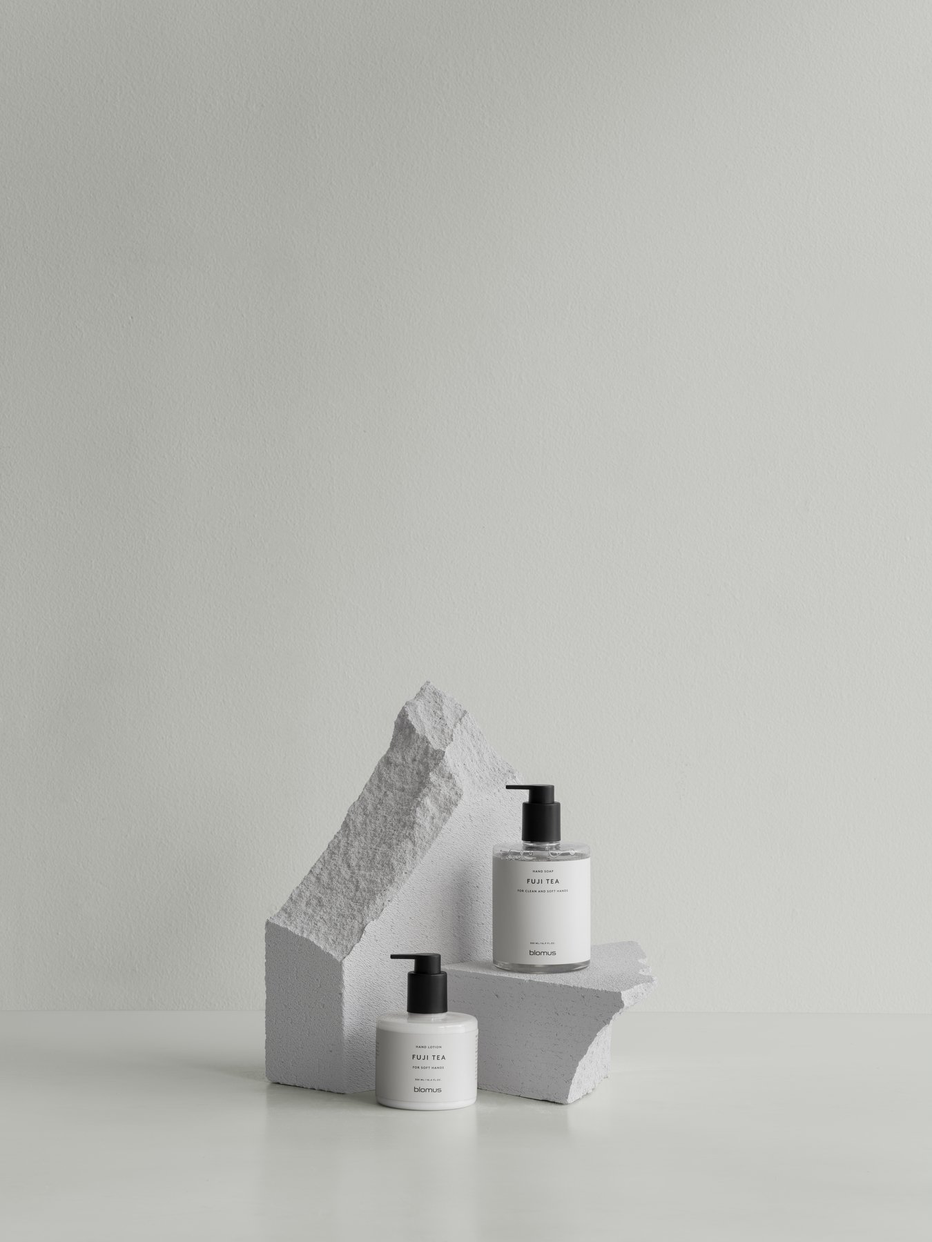 Minimalistische Hautpflegeprodukte, die auf geometrischen Steinformen vor einem hellen Hintergrund präsentiert werden.