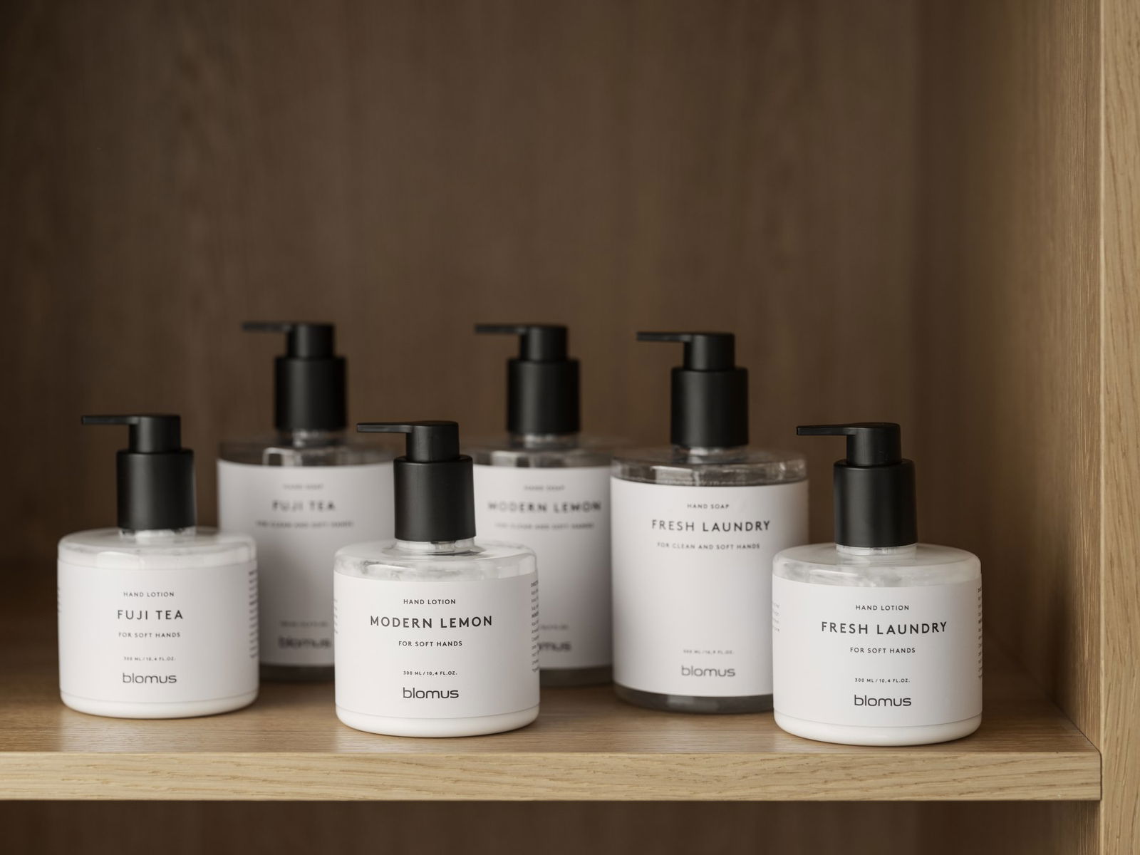 Stylish hand lotions in pump bottles on a wooden shelf for soft, clean hands.