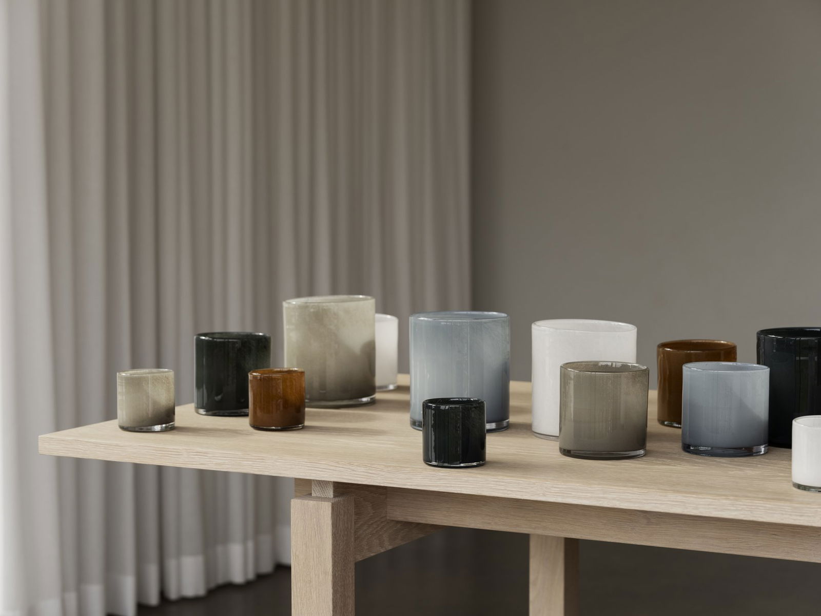 Stylish decorative glass candles in various colors arranged on a wooden table.