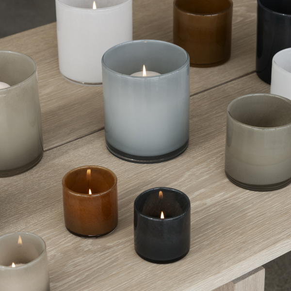 Eine Vielzahl von beleuchteten Kerzen in Glasbehältern auf einem Holztisch, die eine warme Atmosphäre schaffen.