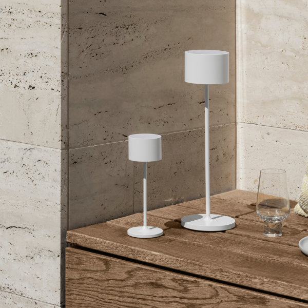 Zwei moderne weiße Tischlampen auf einer Holzoberfläche mit einem dekorativen Glas in einem eleganten Raum.