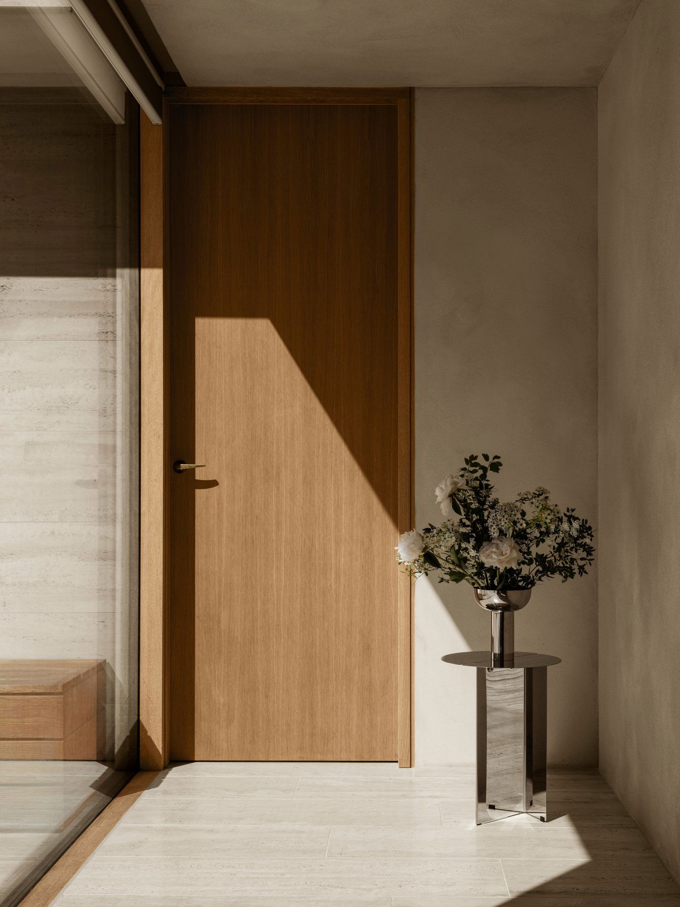 Modernes Interieur mit einer Holztür und einer minimalistischen Vase mit Blumen.