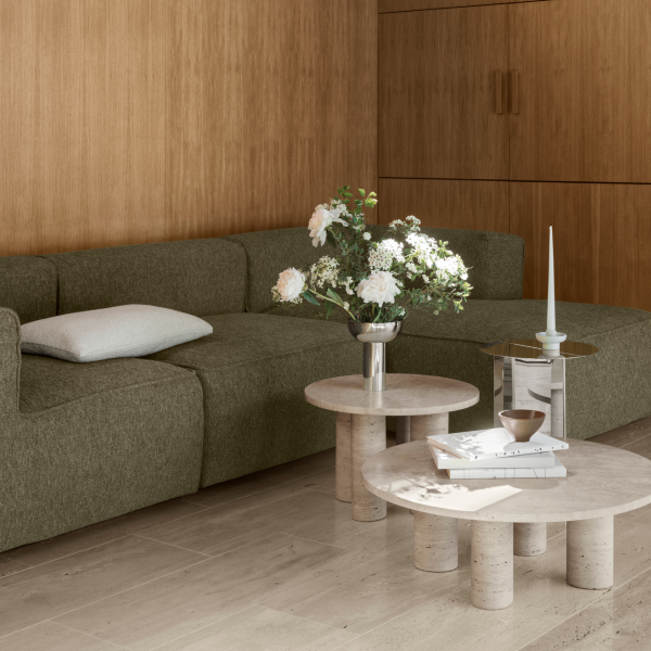 Modernes Wohnzimmer mit einem grünen Sofa, Marmortischen und frischen Blumenarrangements.