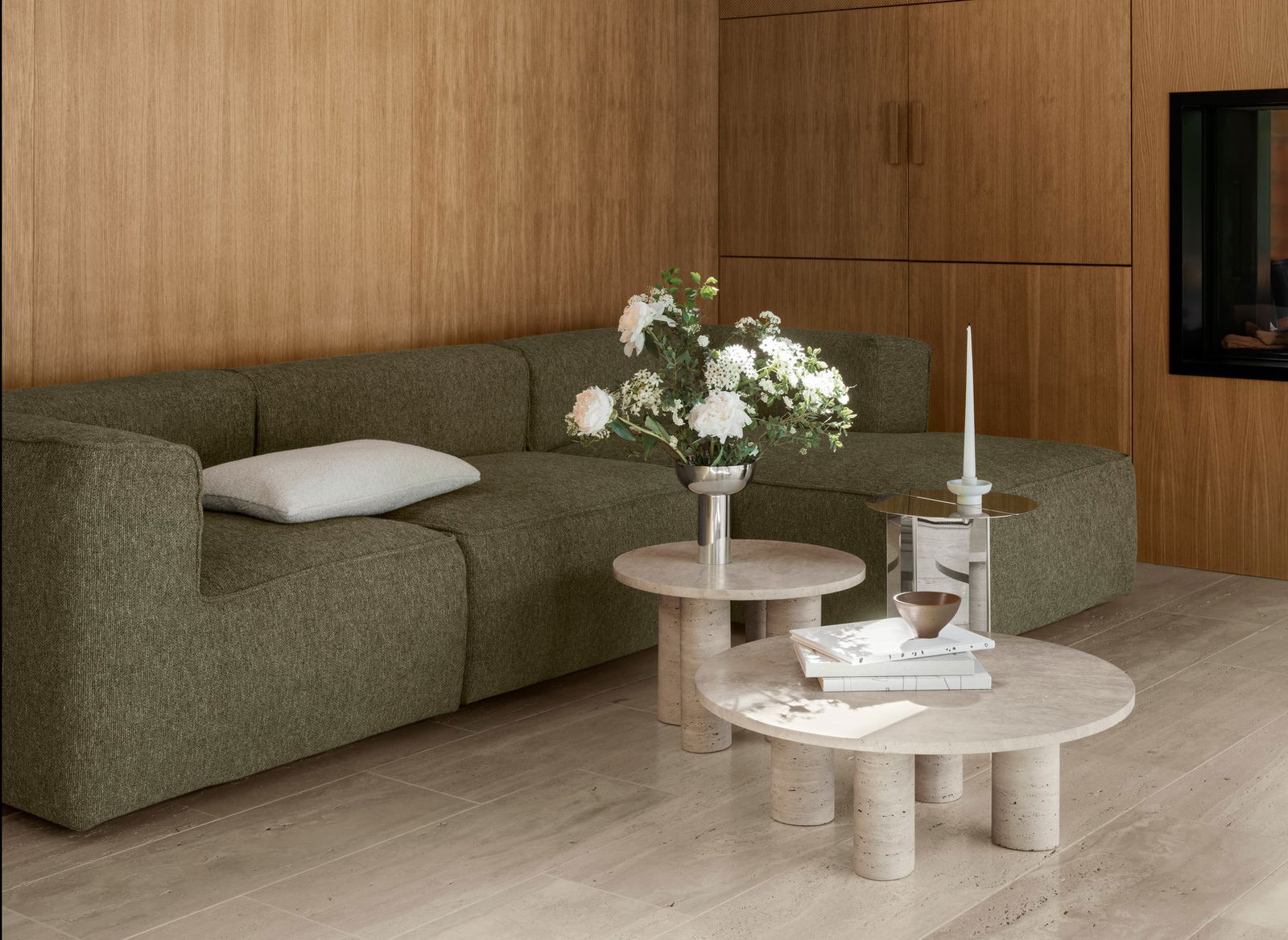 Modernes Wohnzimmer mit einem grünen Sofa, Marmortischen und frischen Blumenarrangements.