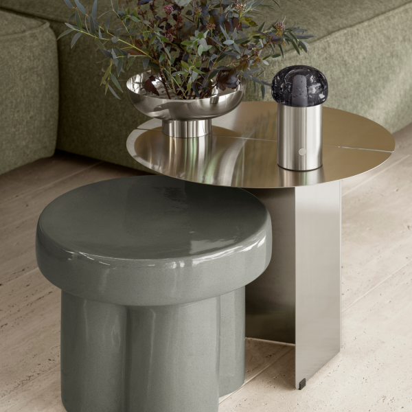 Zeitgenössischer Wohnraum mit einem metallischen Beistelltisch und einem eleganten Hocker mit einer Vase.