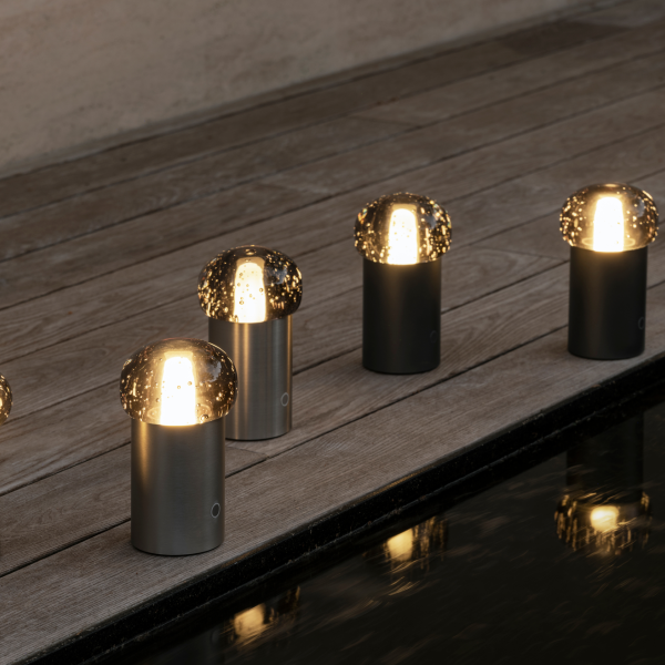 Moderne Außenpilzlichter beleuchten eine Holzterrasse am Wasser.