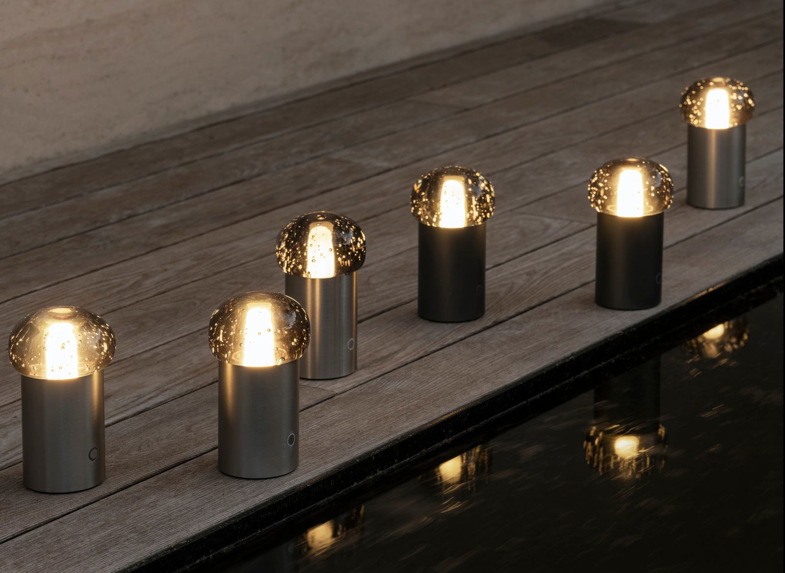 Moderne Außenpilzlichter beleuchten eine Holzterrasse am Wasser.