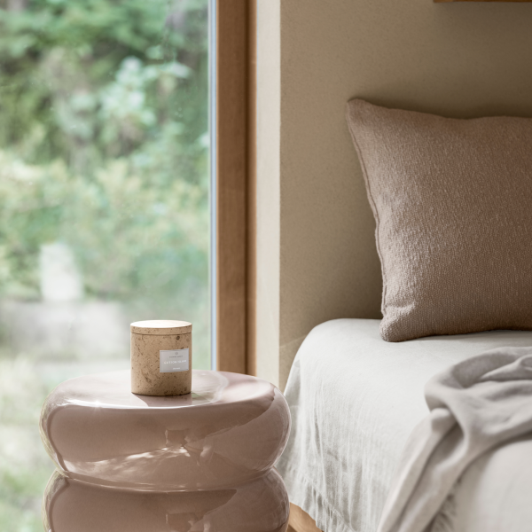 Cozy bedroom corner with a candle on a modern glass side table and soft bedding.