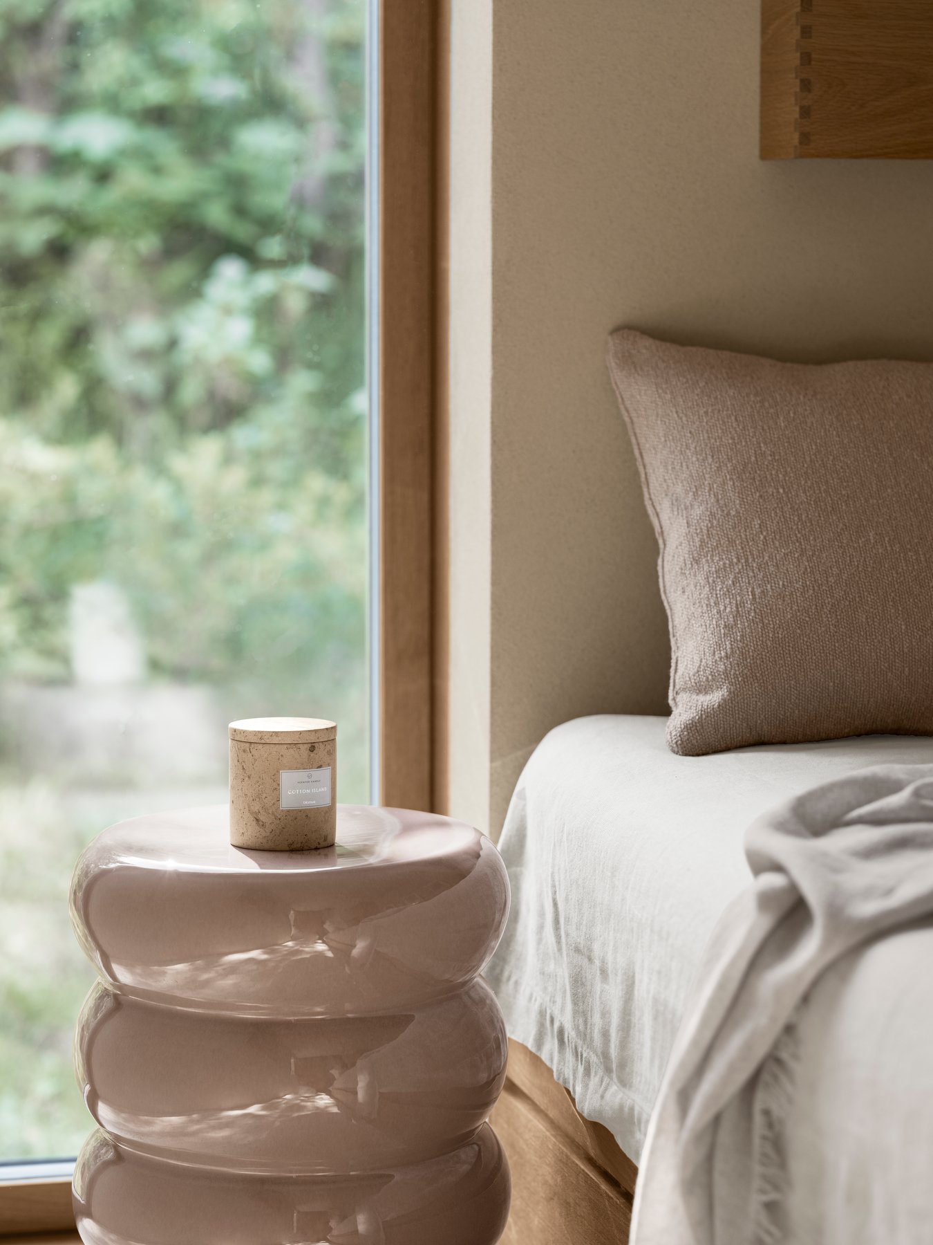 Cozy bedroom corner with a candle on a modern glass side table and soft bedding.