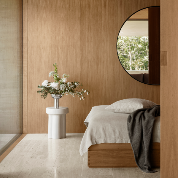 Elegantes Schlafzimmer mit Holzdecken, rundem Spiegel und einem Blumenzentrum auf einem Beistelltisch.