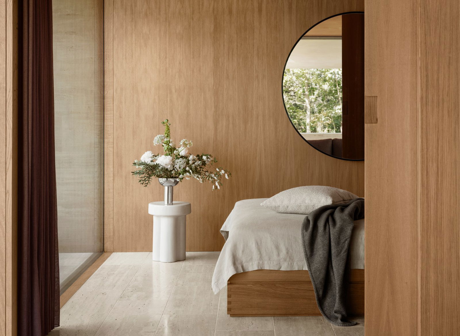 Elegantes Schlafzimmer mit Holzdecken, rundem Spiegel und einem Blumenzentrum auf einem Beistelltisch.