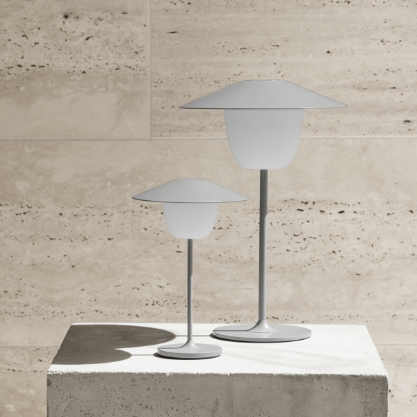 Moderne weiße Tischlampen auf einem Betonpodest vor einem strukturierten Stein Hintergrund.