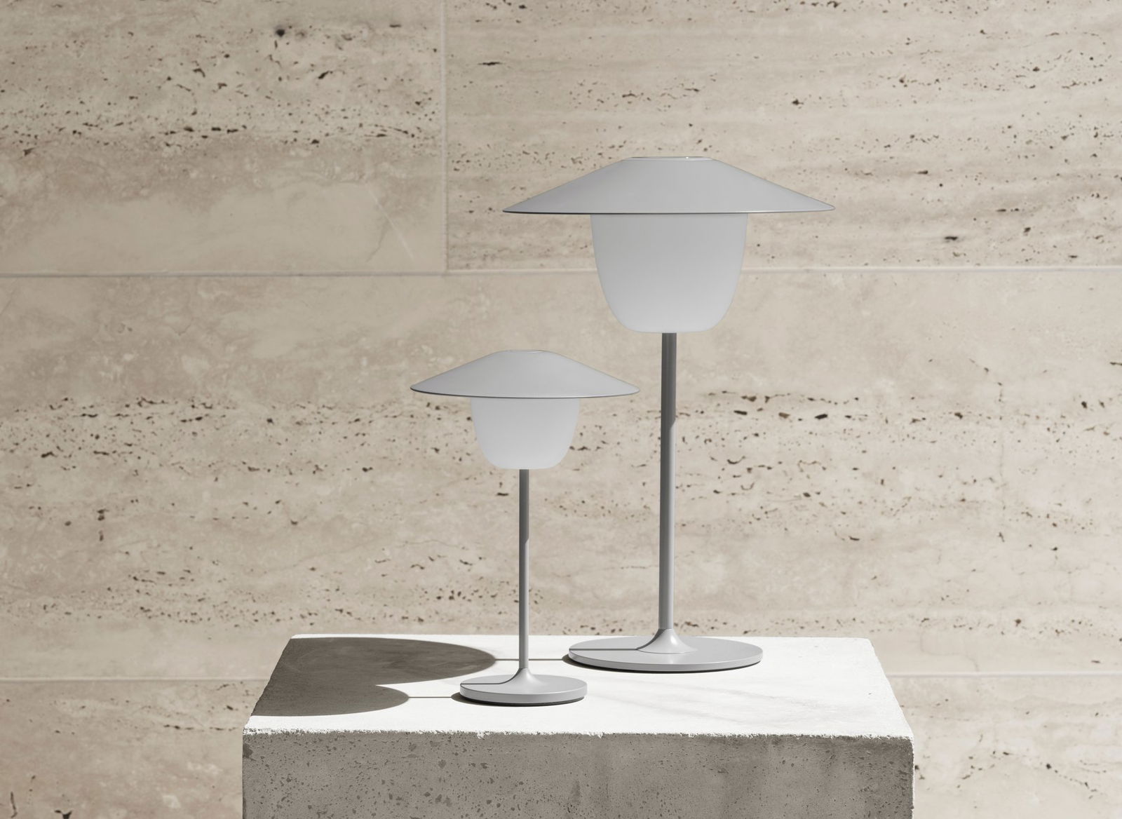 Moderne weiße Tischlampen auf einem Betonpodest vor einem strukturierten Stein Hintergrund.