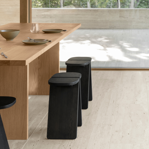 Modern dining space with a wooden table and minimalist black stools in a serene setting.