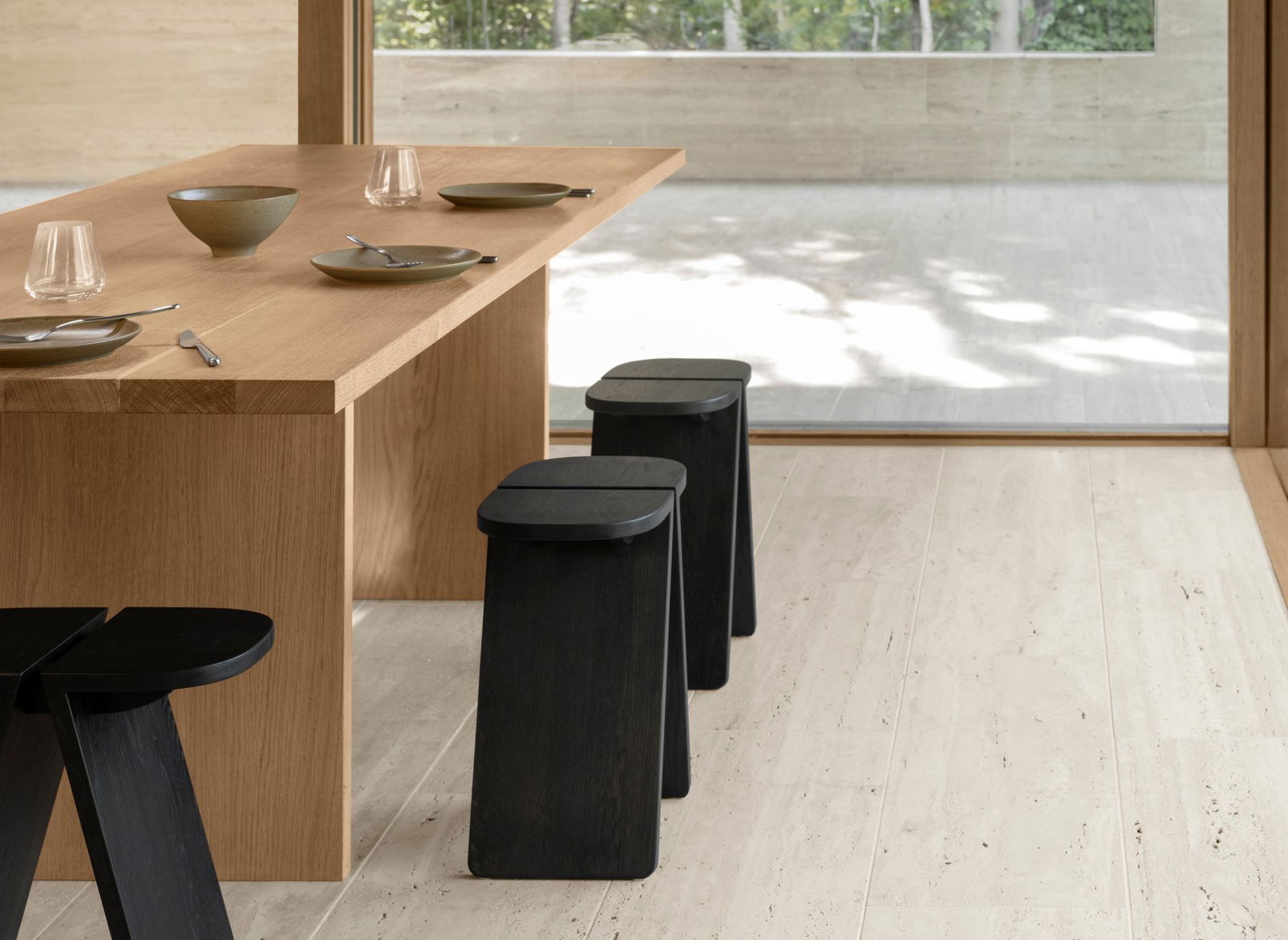 Modern dining space with a wooden table and minimalist black stools in a serene setting.