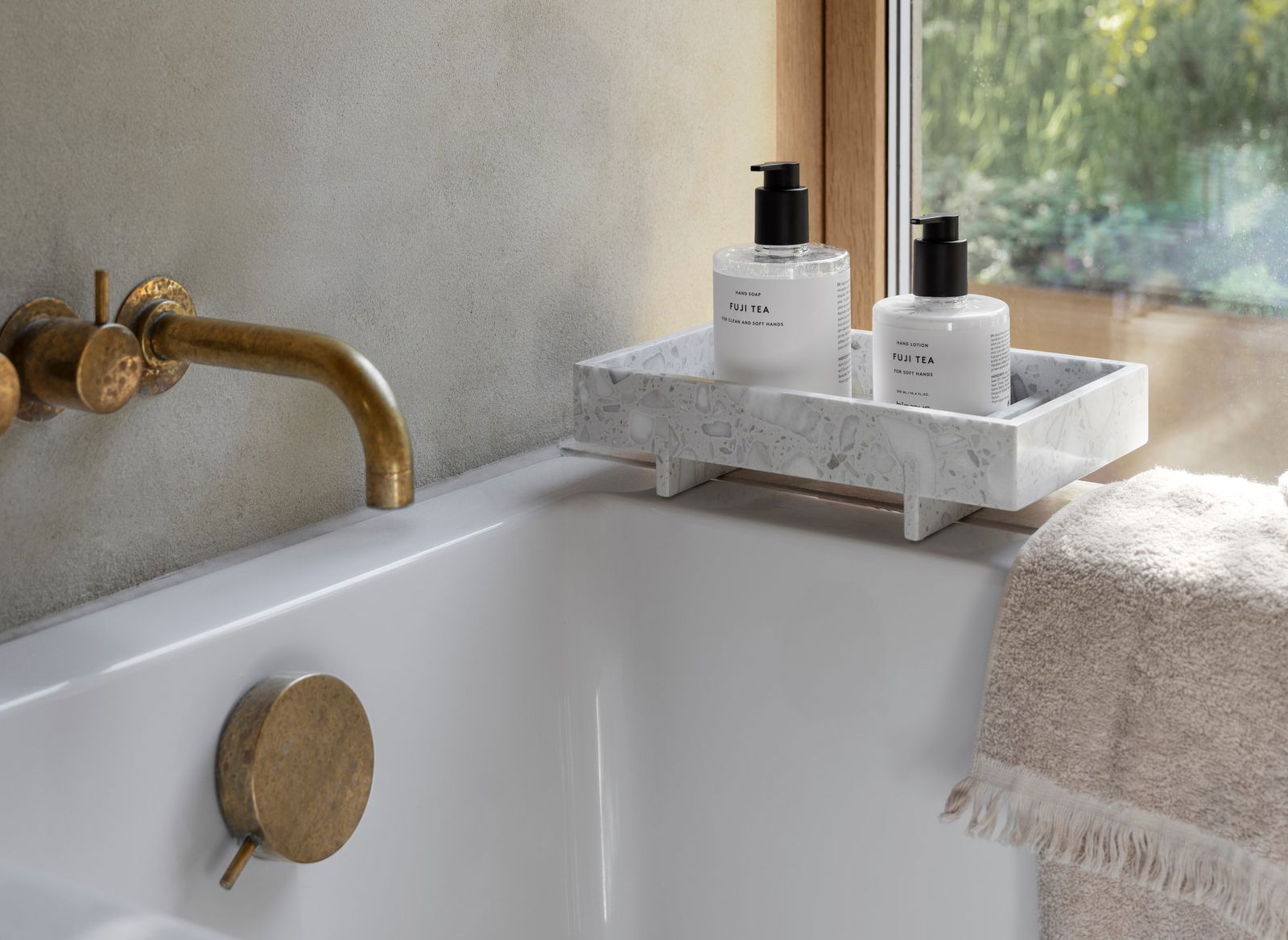 Elegante Badezimmer-Szene mit FUJI TEA Hautpflegeflaschen auf einem Marmor-Tablett neben einer luxuriösen Badewanne.