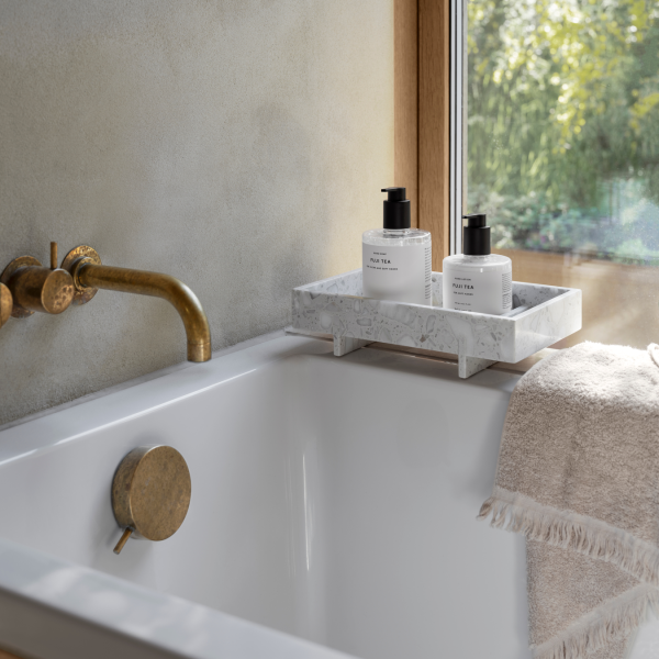 Elegante Badezimmer-Szene mit einem Marmortablett, weichem Handtuch und Hautpflegeprodukten an einem sonnigen Fenster.