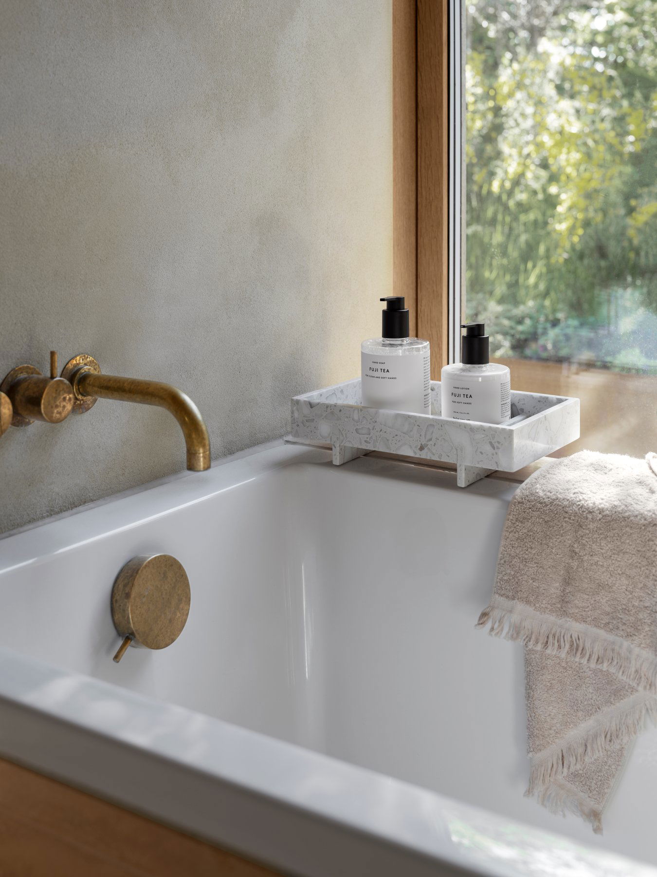 Elegante Badezimmer-Szene mit einem Marmortablett, weichem Handtuch und Hautpflegeprodukten an einem sonnigen Fenster.