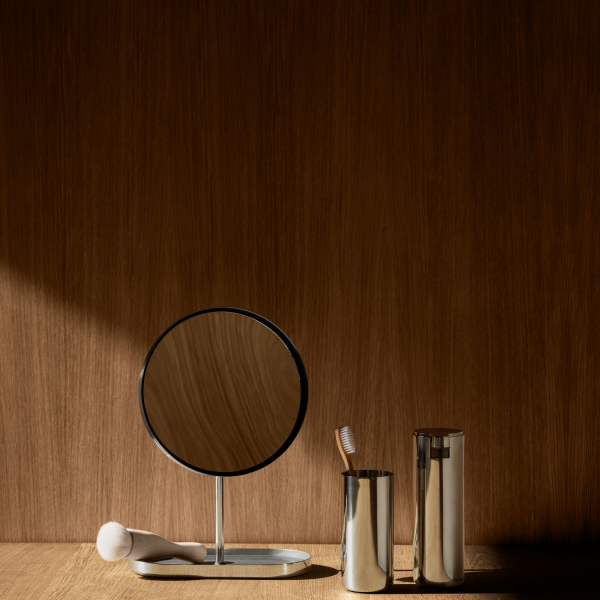 Elegant bathroom setup featuring a mirror and stylish metallic accessories on a wooden background.