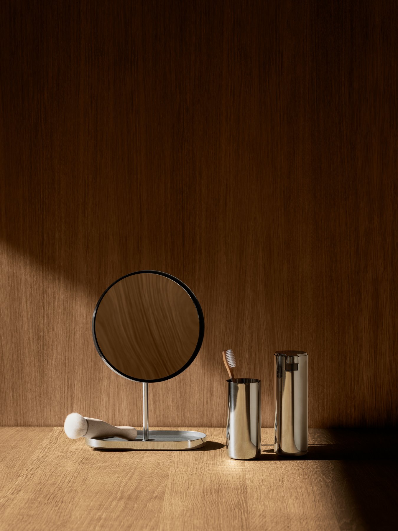 Elegant bathroom setup featuring a mirror and stylish metallic accessories on a wooden background.