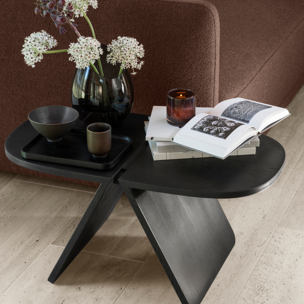 Stylish black side table with flowers, candles, and a book in a cozy living room setting.