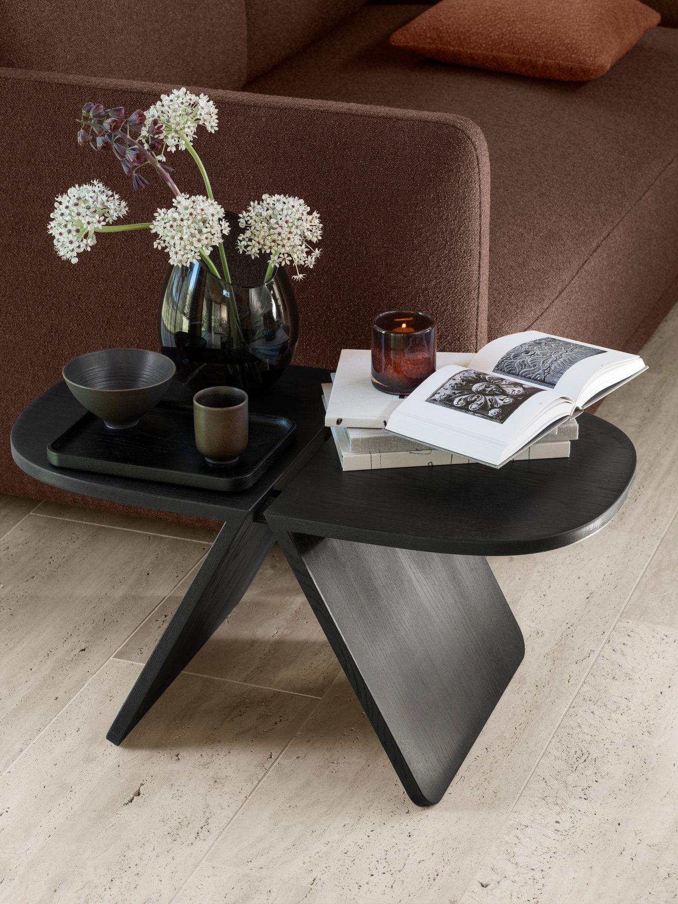 Stylish black side table with flowers, candles, and a book in a cozy living room setting.