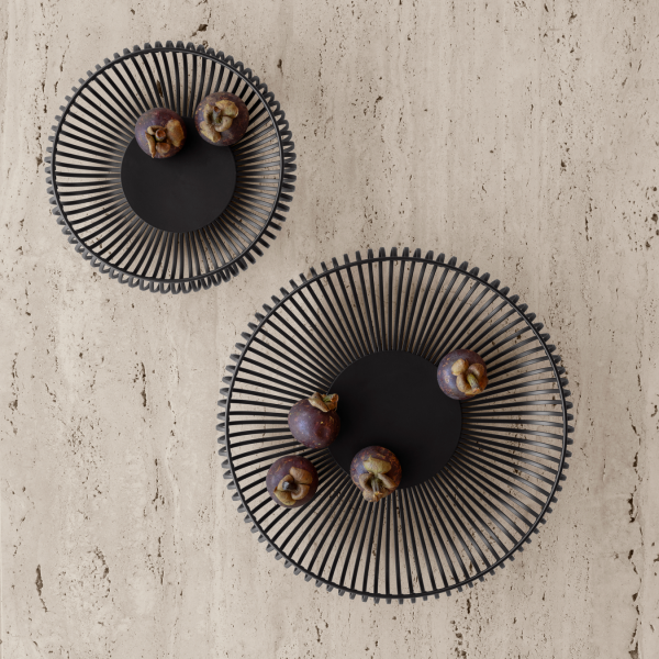 Elegant black wire bowls on a textured surface with fruits arranged artistically.