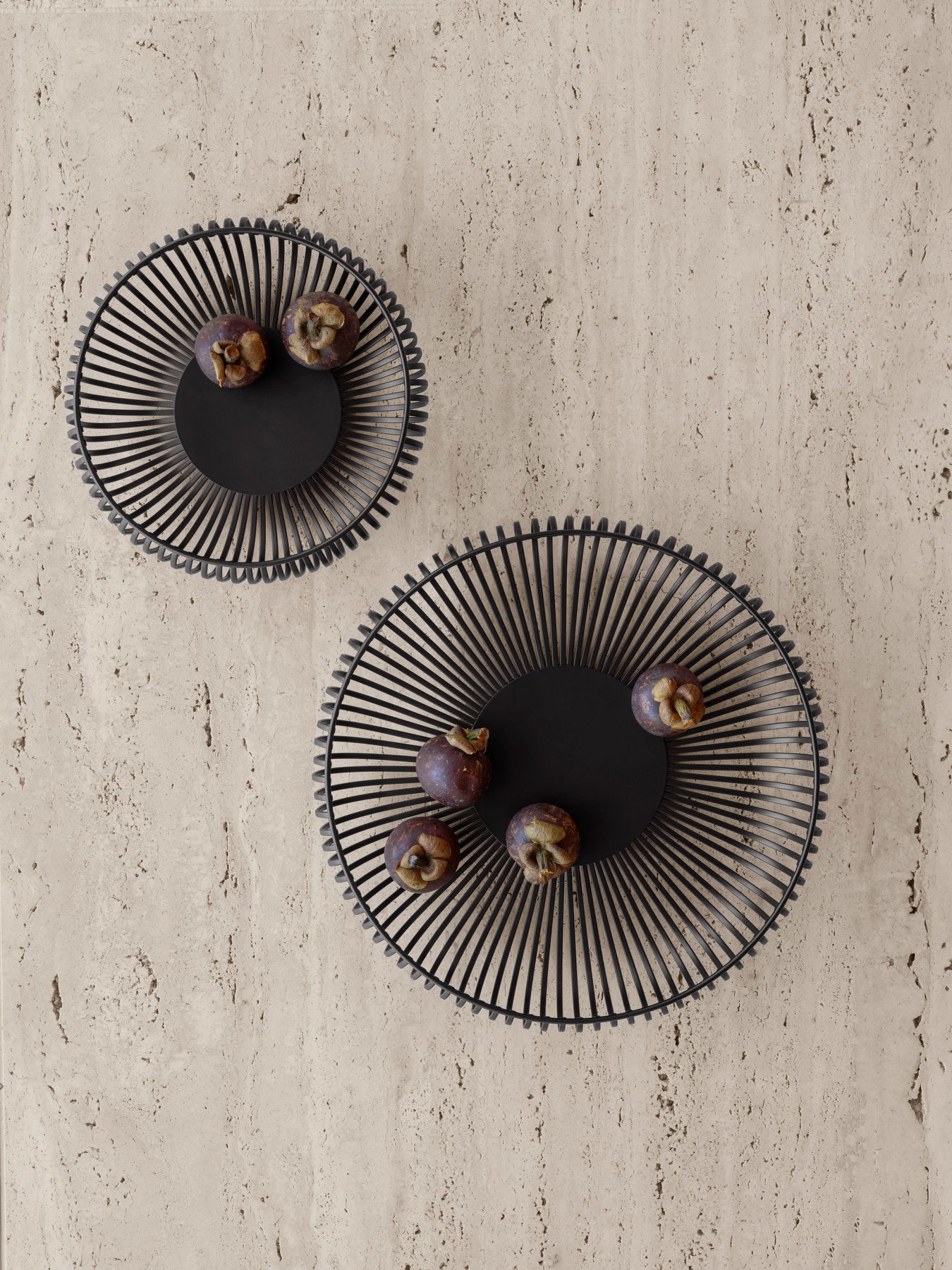 Elegant black wire bowls on a textured surface with fruits arranged artistically.