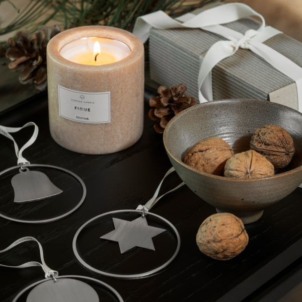 Gemütliche Urlaubsszene mit einer Kerze, Ornamenten, Nüssen und einer Geschenkbox auf einer dunklen Holzoberfläche.