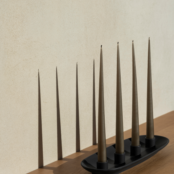 Eleganter Kerzenhalter mit vier konisch geformten Kerzen, die sanfte Schatten an eine strukturierte Wand werfen.