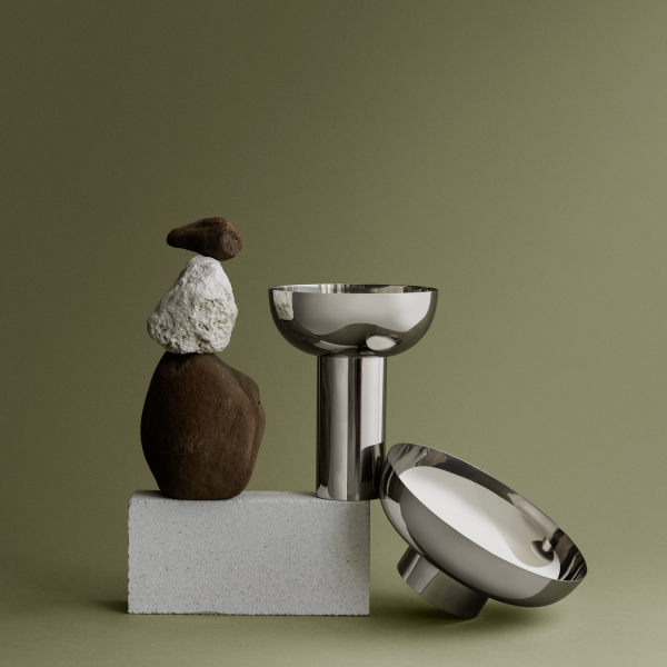 Moderne metallische Schalen, die mit gestapelten Steinen auf einem minimalistischen grünen Hintergrund präsentiert werden.