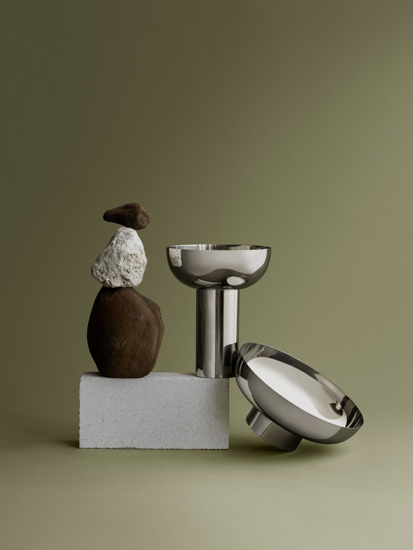 Moderne metallische Schalen, die mit gestapelten Steinen auf einem minimalistischen grünen Hintergrund präsentiert werden.