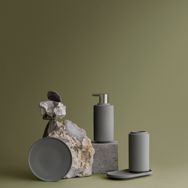 Stylish gray bathroom accessories displayed on stone with a minimalist green background.