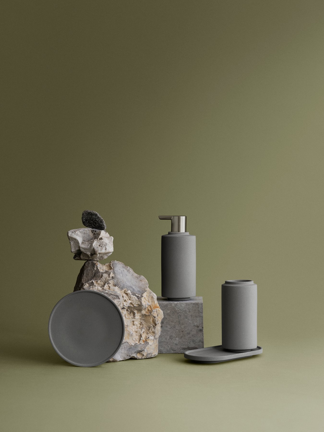 Stylish gray bathroom accessories displayed on stone with a minimalist green background.