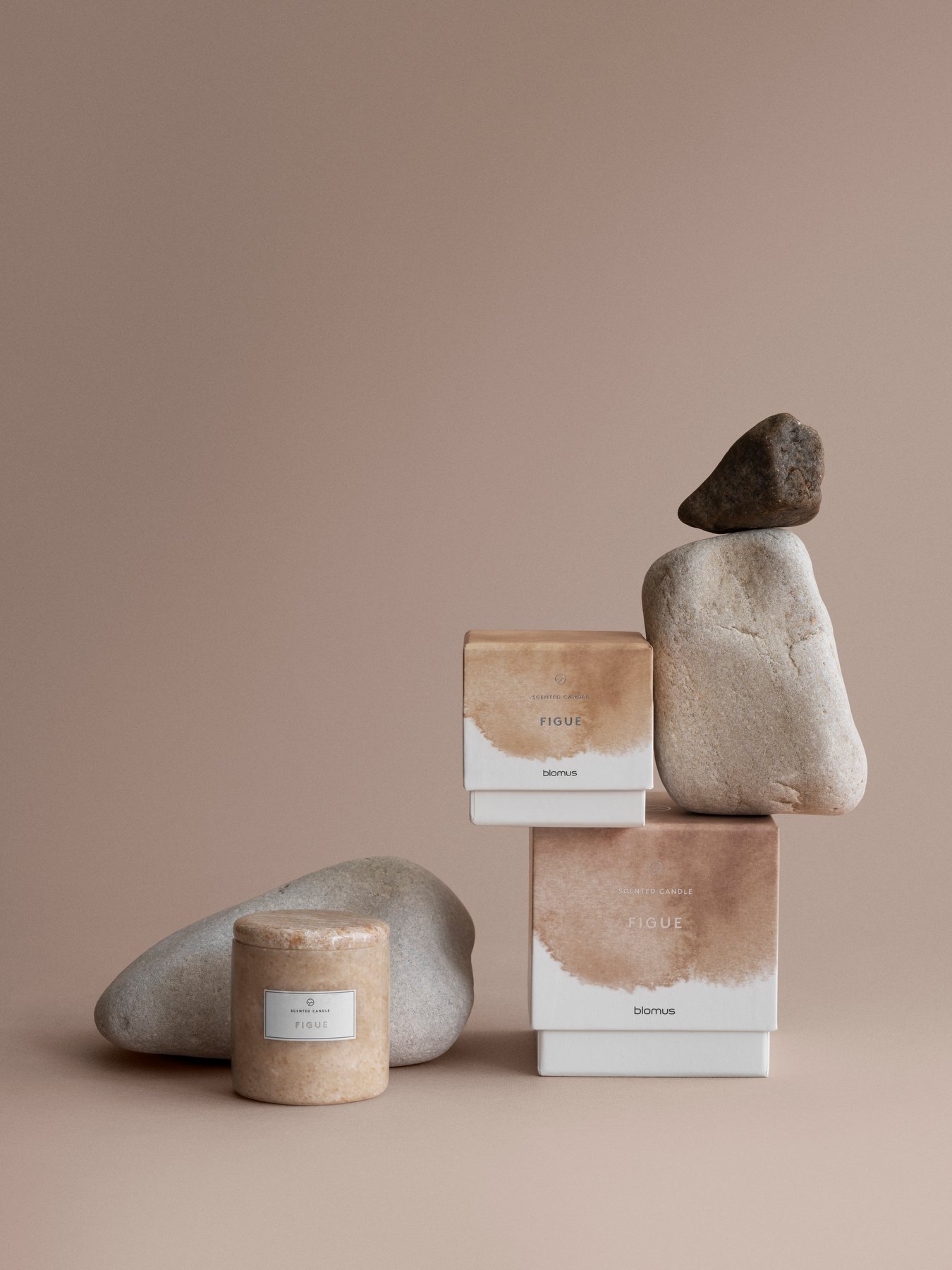 Natural stone and fig-scented products displayed on a soft beige background.