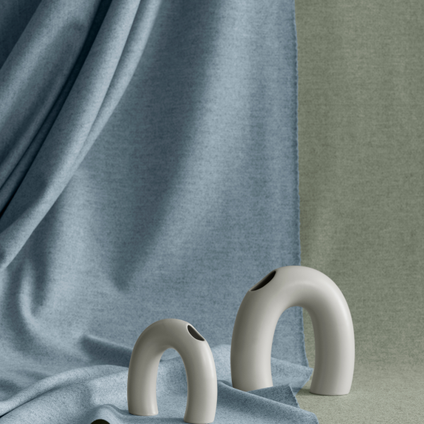 Minimalist ceramic vases on textured fabric backdrop in soft blue and green tones.
