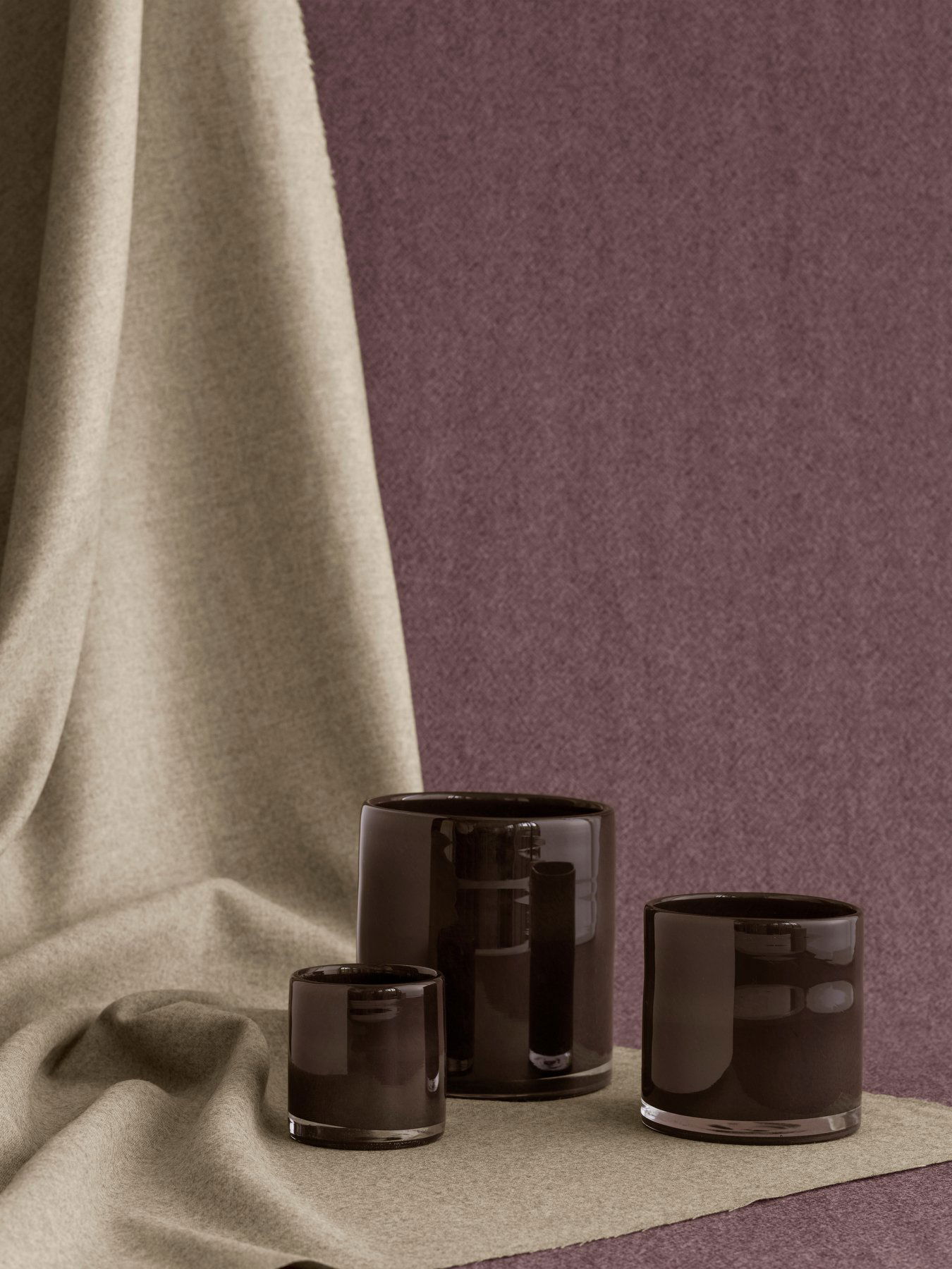 Elegante schwarze Glas-Teelichthalter vor einem strukturierten Stoffhintergrund.