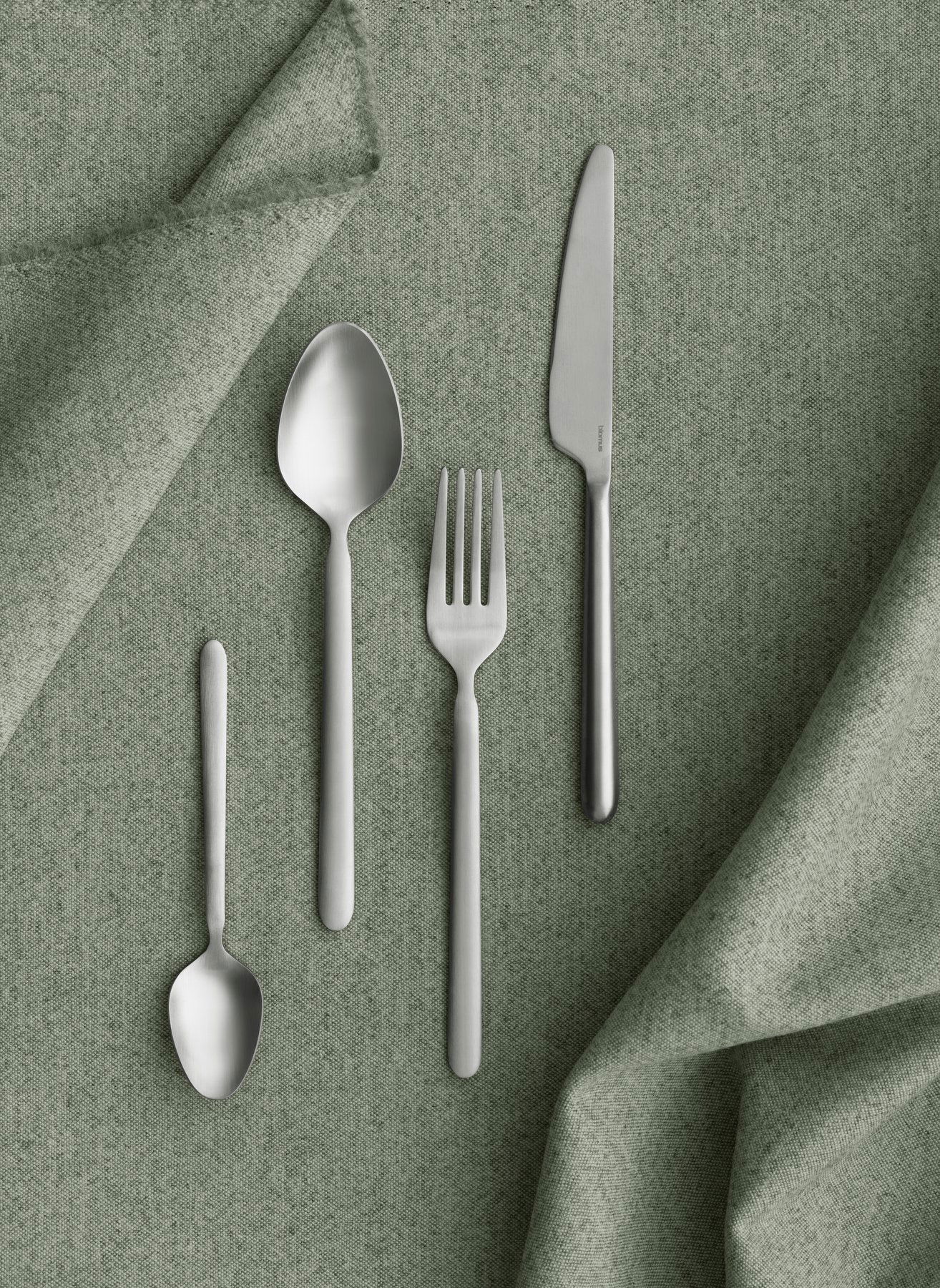 Elegantes silbernes Besteckset auf einem strukturierten grünen Stoffhintergrund.