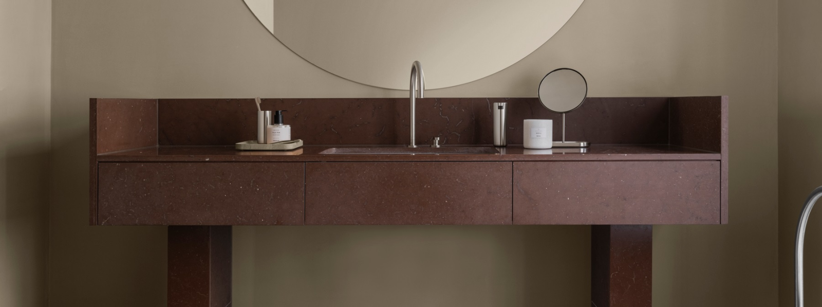 Modern bathroom vanity with a round mirror, sink, and stylish accessories in earthy tones.