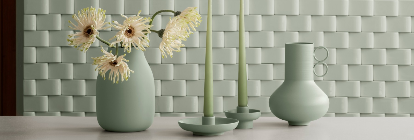 Elegante mintgrüne Vasen und Kerzenständer mit Blumenarrangement auf einem Tisch.