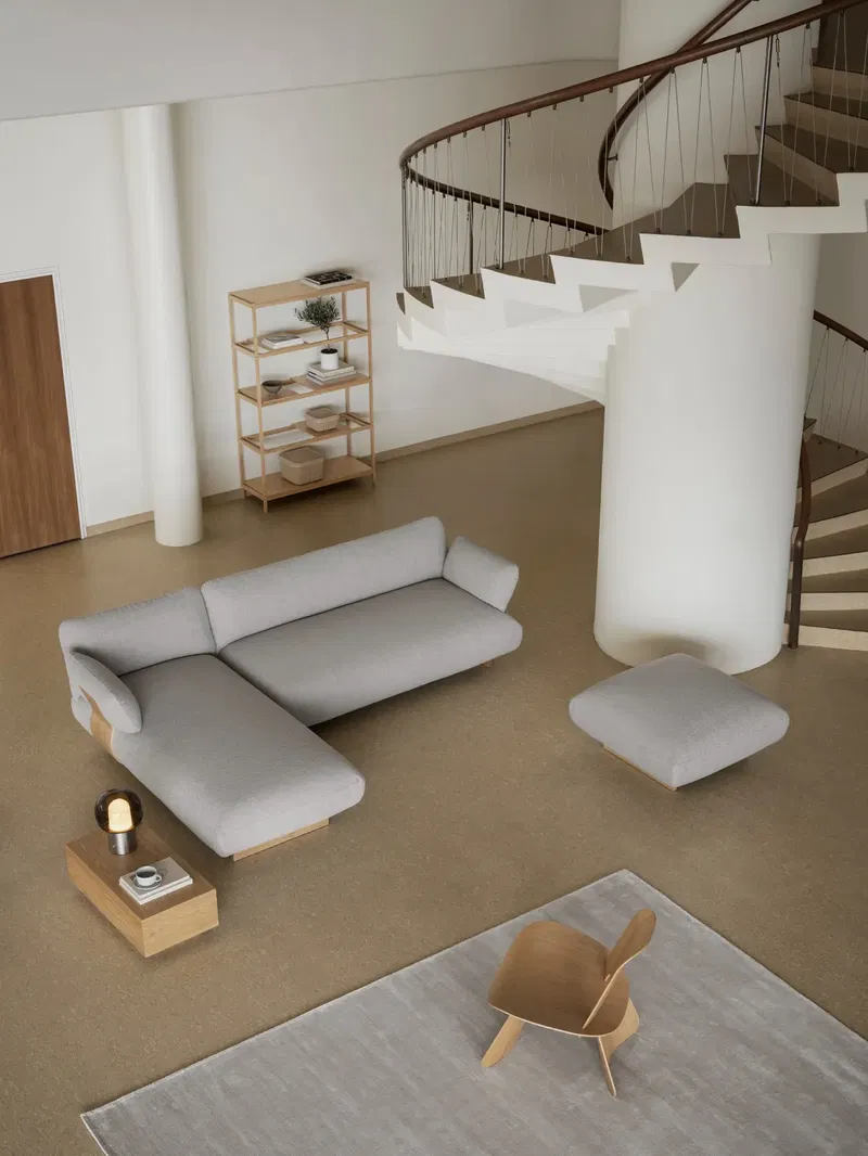 Moderne Wohnraumgestaltung mit grauem Sofa, minimalistischen Möbeln und Treppenhaus.