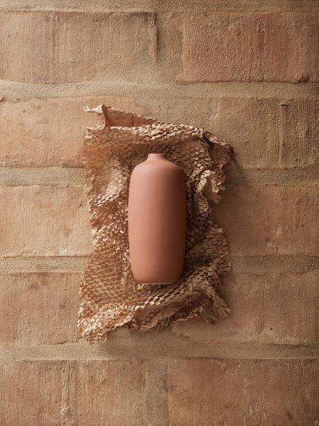 Minimalist clay vase on textured paper against a rustic brick background.