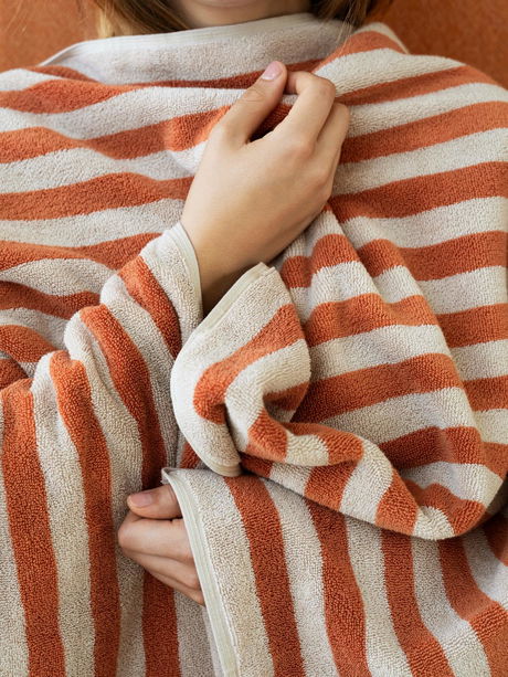 Cozy hands wrapped in a soft striped towel against an earthy background.